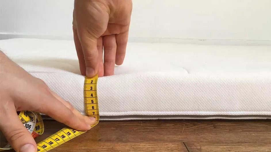 Testing Cot Mattress Firmness Hand pressing and measuring a white cot mattress to check firmness and support for safe baby sleep.